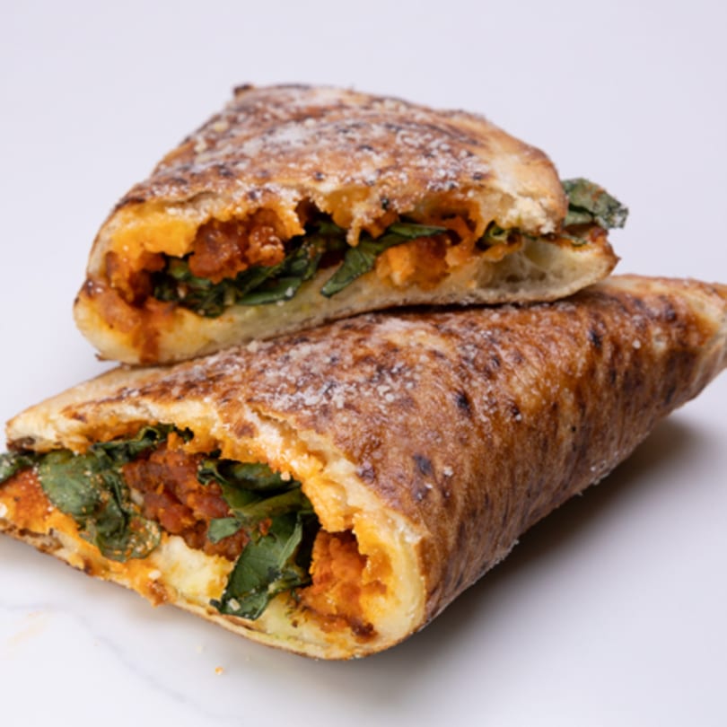 Two halves of a calzone filled with orange sauce, green spinach, and cheese, dusted with parmesan.