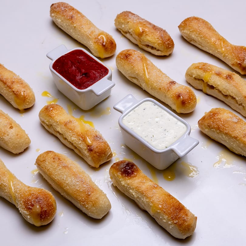 Pizza Place breadsticks with honey, parmesan, marinara, and ranch dipping sauces on a white surface.