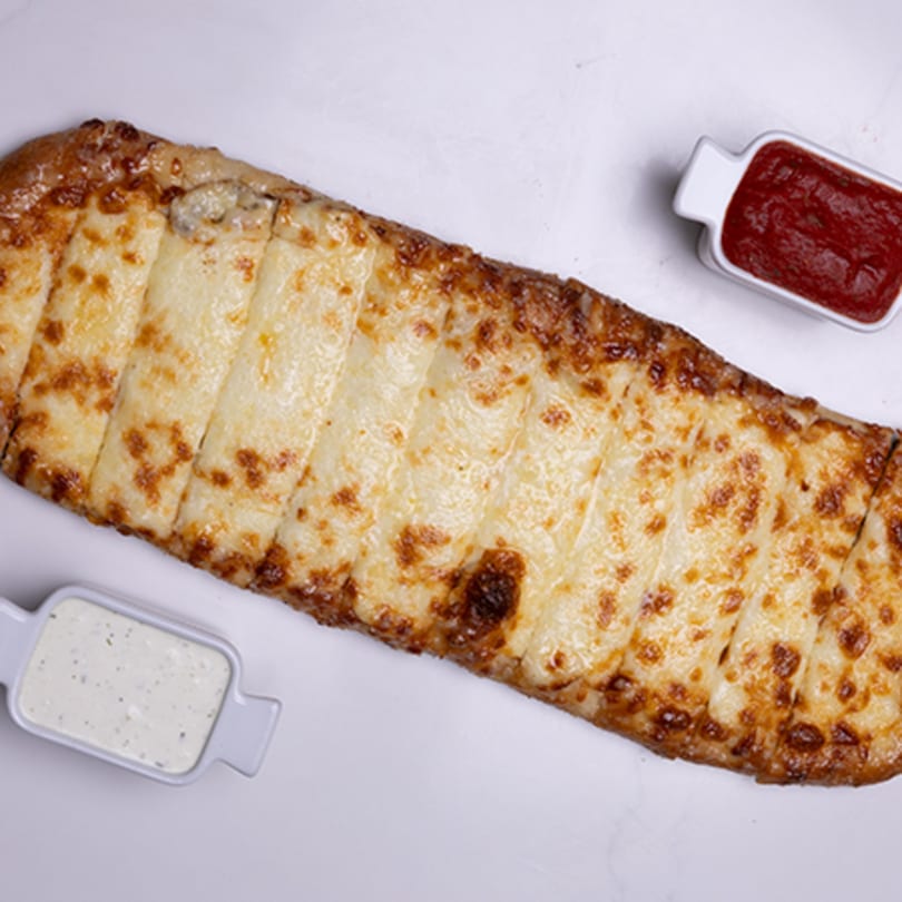 Long, rectangular cheesy breadsticks, cut into strips, with small dishes of red and white dipping sauces.