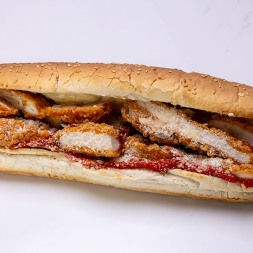 A close-up of a chicken parmesan hero sandwich with red sauce and grated cheese.