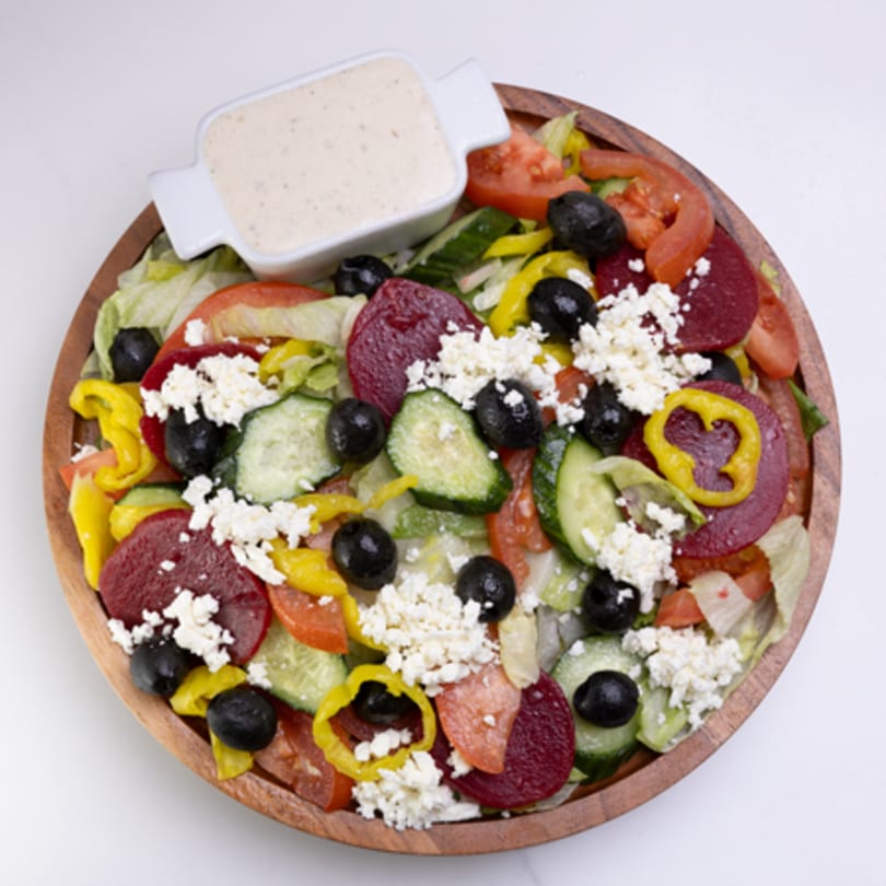 Colorful salad with lettuce, tomatoes, cucumbers, olives, beets, banana peppers, and feta cheese.